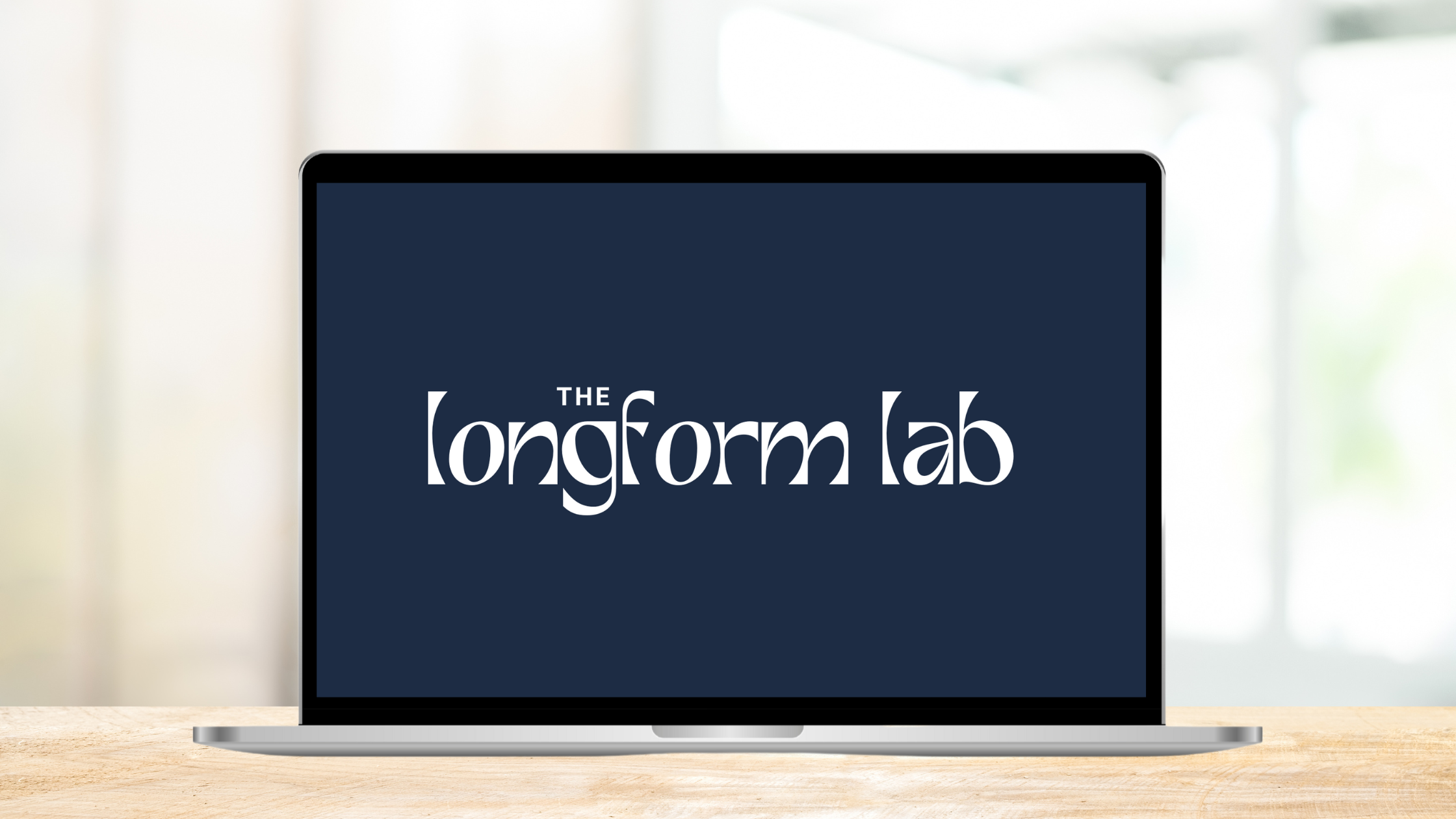 A laptop on a desk, displaying "the Longform Lab" in white text on a blue background.